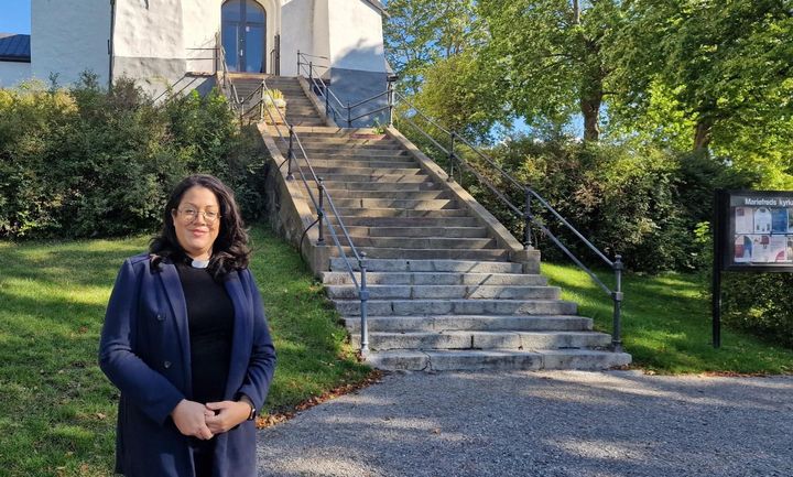 Kvinna med prästkrage framför kyrka.