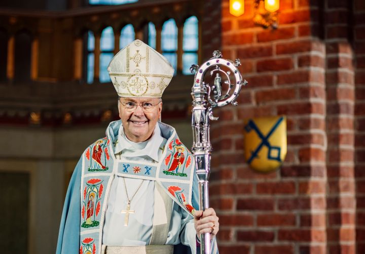 Biskop Johan Dalman i liturgisk klädsel med mitra och kräkla, i domkyrkan framför en tegelvägg med stiftets vapen på.