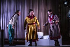 Tre personer i färgglada samiska kläder står på en scen med draperi i bakgrunden.