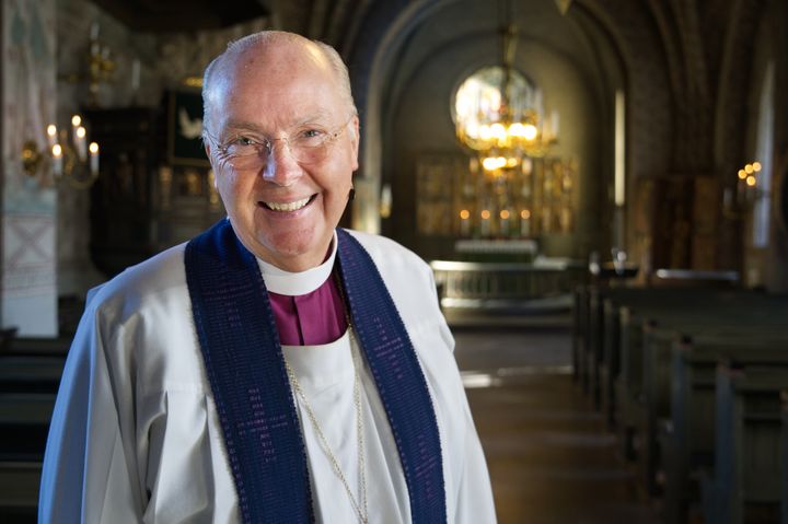 Glad äldre manlig biskop i liturgiska kläder står inuti en kyrka