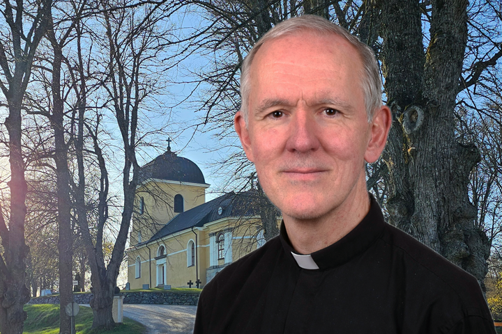 En manlig präst framför en gul kyrka omgiven av träd.