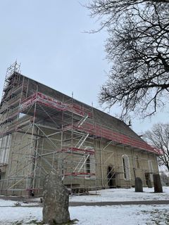 Grå stenkyrka med byggnadsställningar för takrenovering