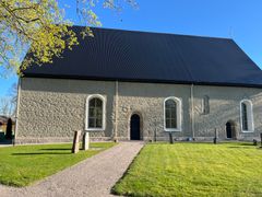 Bild på Sköllersta kyrka med nytt svart plåttak och en solig grön omgivning.