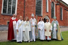 Präster, diakoner och biskopar i liturgiska kläder framför katedral i rött tegel.