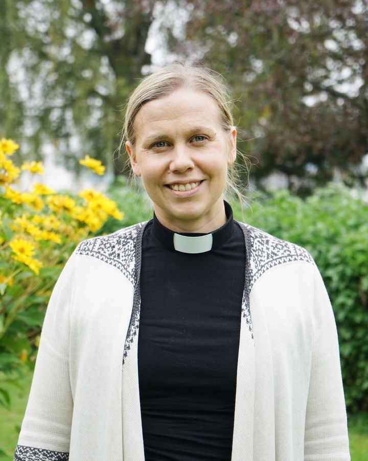 Porträtt av Linda Wallgren, ny kyrkoherde i Hallsbergs församling, utomhus framför gröna och blommande buskar.