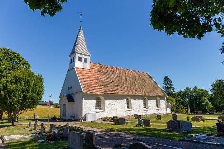 Bälinge kyrka i en sommarklädd omgivning. Fotografiet är taget av Stefan Lindberg och man ser kyrkan från sidan.