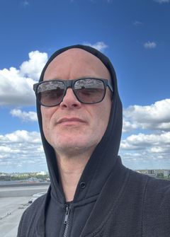 Porträtt av Stefan Viterstedt i svart hoodie och solglasögon under blå himmel.
