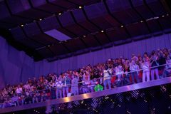 Publik i konsertsalong som applåderar stående, med blått scenljus och vågformat innertak.