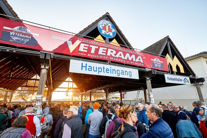 The photo shows the main entrance to VETERAMA at the Maimarkt grounds in Mannheim-Europe's largest classic car market. A long line of people has formed in front of the entrance. Visitors eagerly jostle their way toward the entrance, proving the fair's great popularity and appeal. It's a typical start to an exciting day full of automotive treasures.