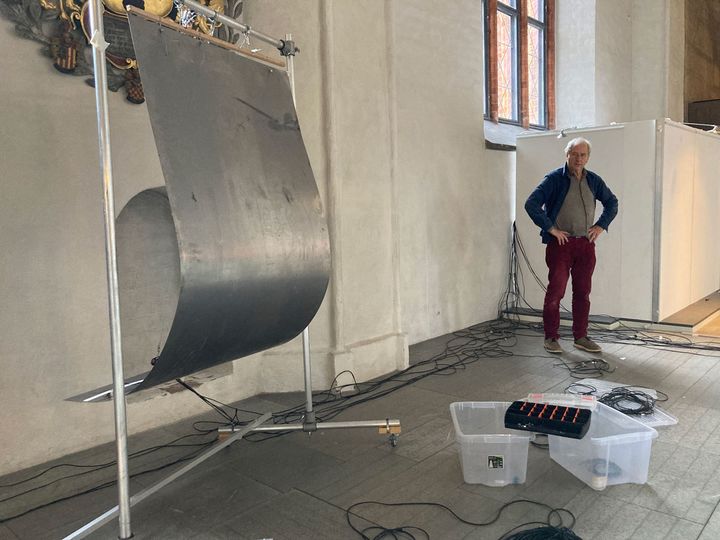 Hängande plåtskiva och sladdar i Västerås domkyrka. Musikern Torbjörn Grass står i bakgrunden.