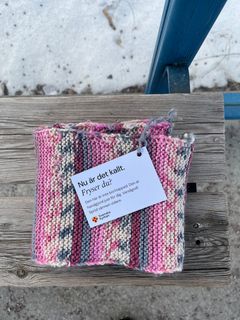 En rosa randig halsduk ligger på en bänk i busshållplatsens vindskydd.