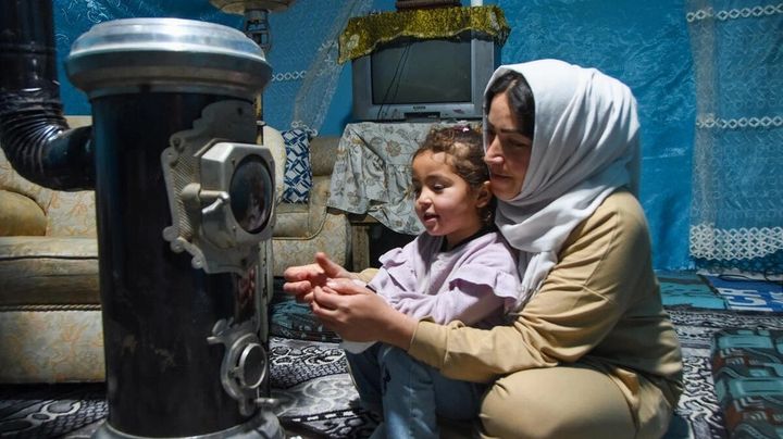 Den syriska flyktingen Khadija och hennes dotter värmer sig inne i sitt tält på en bosättning i Libanons Bekaa-dal.