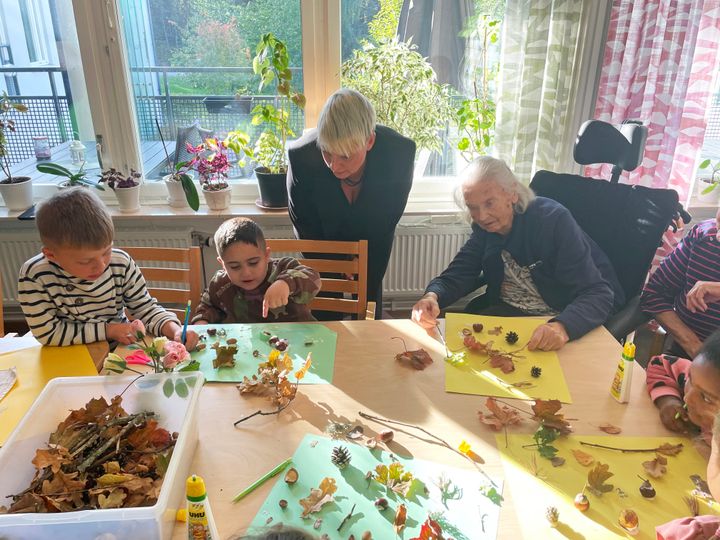 Barn och äldre pysslar runt ett bord med kottar, löv och ekollon.