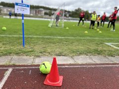 Elever spelar handboll på en gräsplan, uppmärkta stationer syns i bakgrunden.