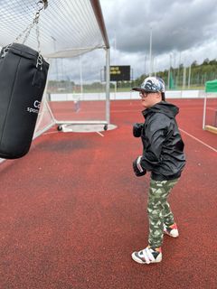 En elev i kamouflagebyxor och keps slår på en boxningssäck på en utomhussportbana.