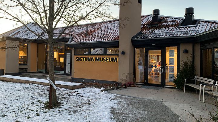 Sigtuna museums entré utifrån. Framför syns ett kalt träd och på marken och taket ligger det lite snö.