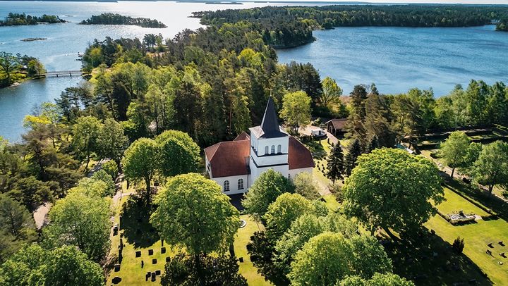 Drönarbild på Påskallaviks kyrka, omgiven av grönska och vatten.