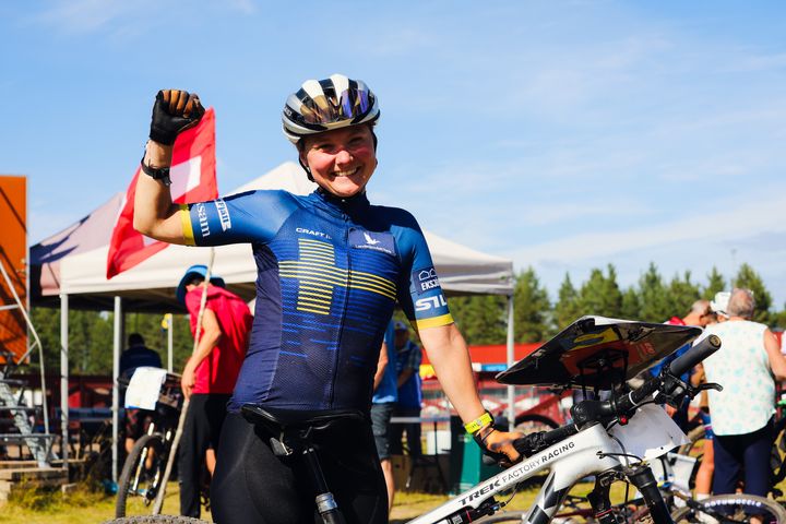 Kvinna i cykelkläder firar med en flagga efter att ha vunnit guld i cykelorientering.