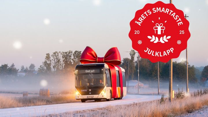 En buss dekorerad som en julklapp kör på en dimmig landsväg. En röd etikett med texten "Årets smartaste julklapp 2025" syns i hörnet.
