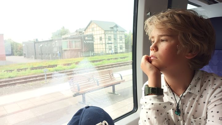 Pojke med avslappnat uttryck tittar ut genom ett tågfönster.