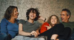 Glad familj med tonårsbarn hemma i soffan.