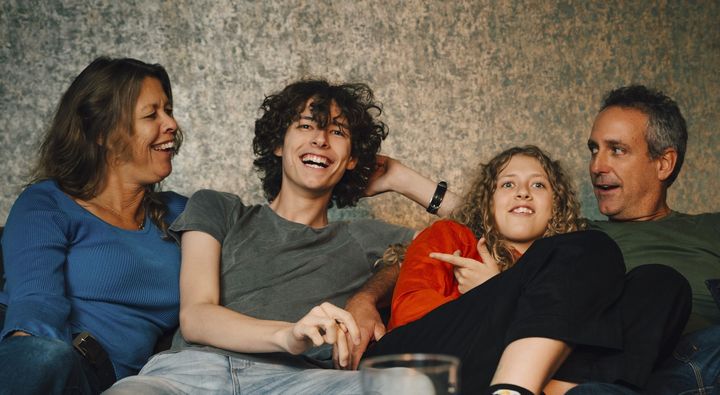 Glad familj med tonårsbarn hemma i soffan.