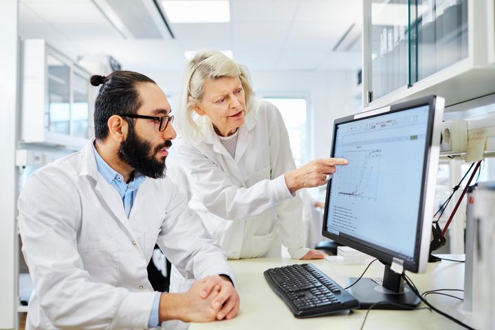 En man och en kvinna i vita rockar framför en datorskärm som visar ett diagram