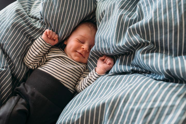 Nyfödd nöjd bebis sover i säng i hemmamiljö