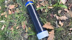 En tom lustgasbehållare ligger på marken bland gräs och löv.