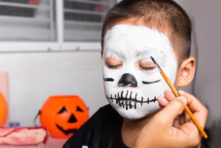 Bild på ett barn som får ansiktet målat som en skelettmask inför Halloween.