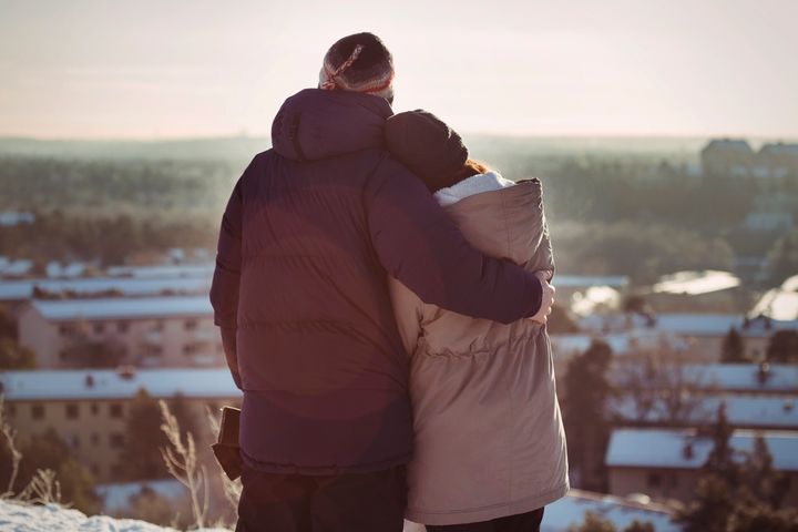 Två personer står och kramar varandra, med utsikt över en stad på vintern.