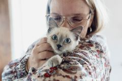 En person håller en kattunge med blå ögon nära sitt ansikte.