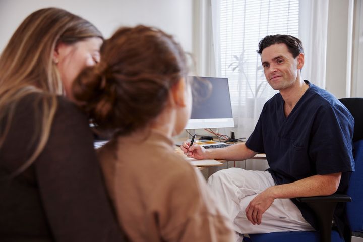 Alt-text: Läkare i samtal med ett barn och en vuxen på en mottagning.