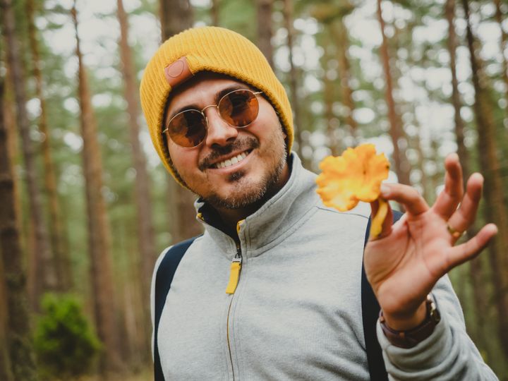 En person med gul mössa och solglasögon håller i en kantarell i en skog.