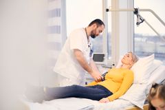 En läkare undersöker en patient som ligger i en sjukhussäng.