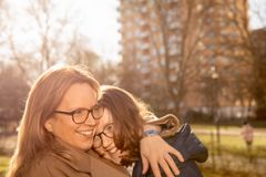 Mor och barn omfamnar varandra leende i en solig park.