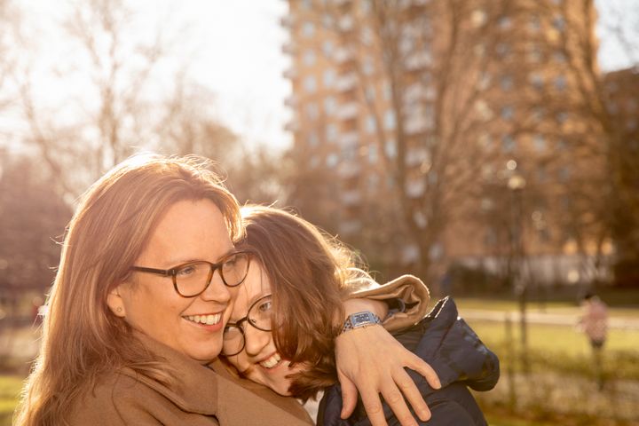 Mor och barn omfamnar varandra leende i en solig park.