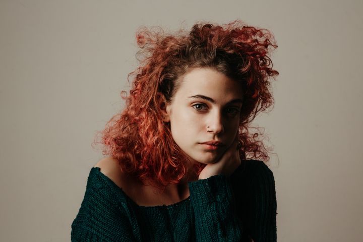 Ung person med lockigt, rött hår och en grön tröja, sitter och ser tankfull ut.
