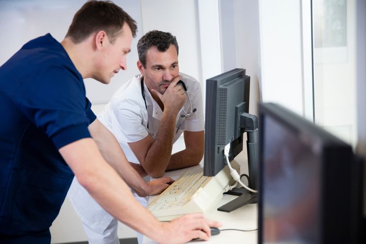 Två män i arbetskläder tittar på en datorskärm och diskuterar.