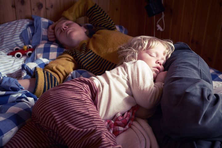 En vuxen och ett barn sover i en säng omgiven av mysiga filtar.