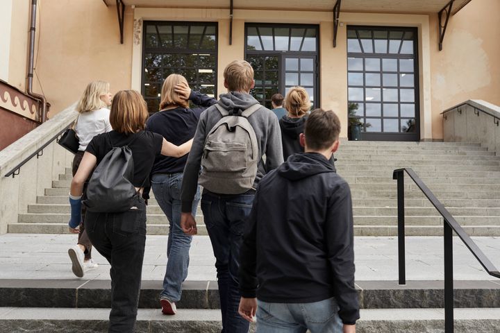En grupp tonåringar går uppför en trappa mot en byggnad som skulle kunna vara en skola.