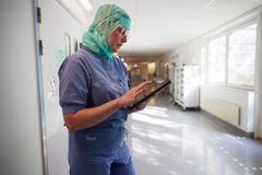 En sjukvårdspersonal klädd i kirurgiska kläder använder en surfplatta i en sjukhuskorridor.