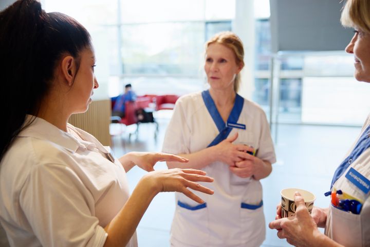 En grupp vårdpersonal samtalar i en ljus sjukhusmiljö.