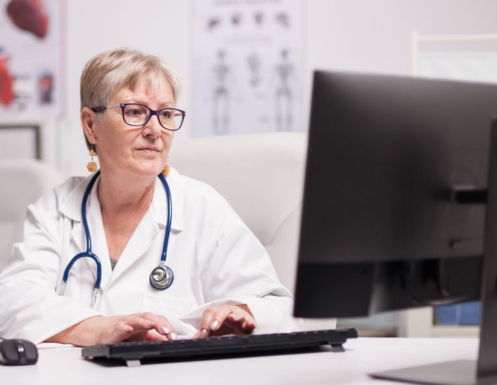 Kvinna i läkarrock sitter vid en dator och skriver.