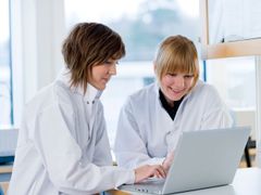 Två personer i vita labbrockar sitter och arbetar vid en bärbar dator.