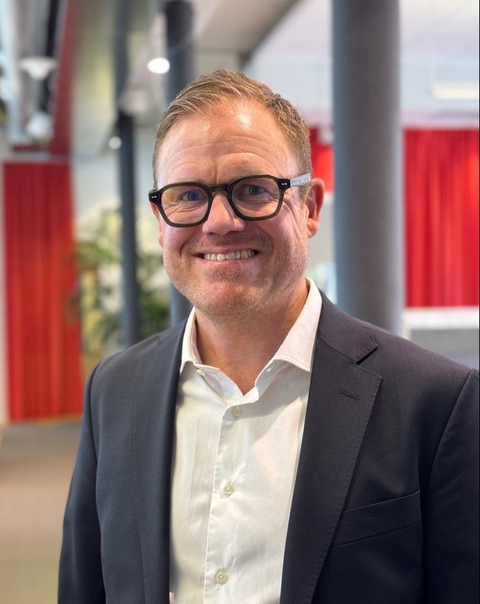 En leende man i kostym som står inomhus.