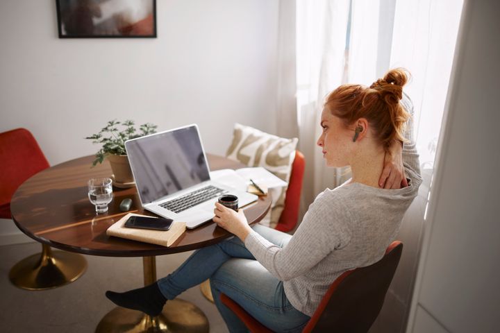 Kvinna sitter vid ett runt bord, arbetar på en laptop och håller en kaffekopp.