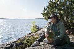 Person som sitter på en klippa vid vattnet och tittar ut över sjön en solig dag.