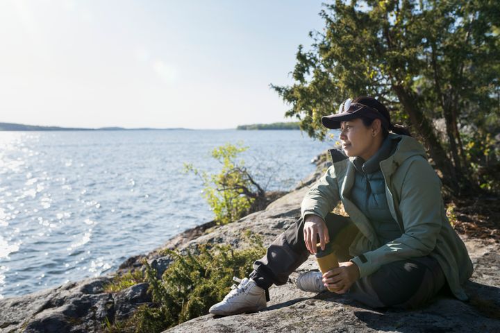 Person som sitter på en klippa vid vattnet och tittar ut över sjön en solig dag.