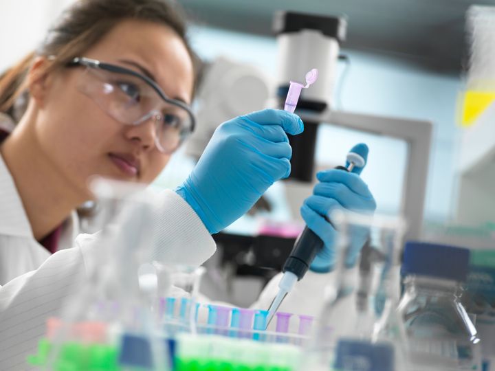 Person i labbrock använder pipett med provrör i ett laboratorium.